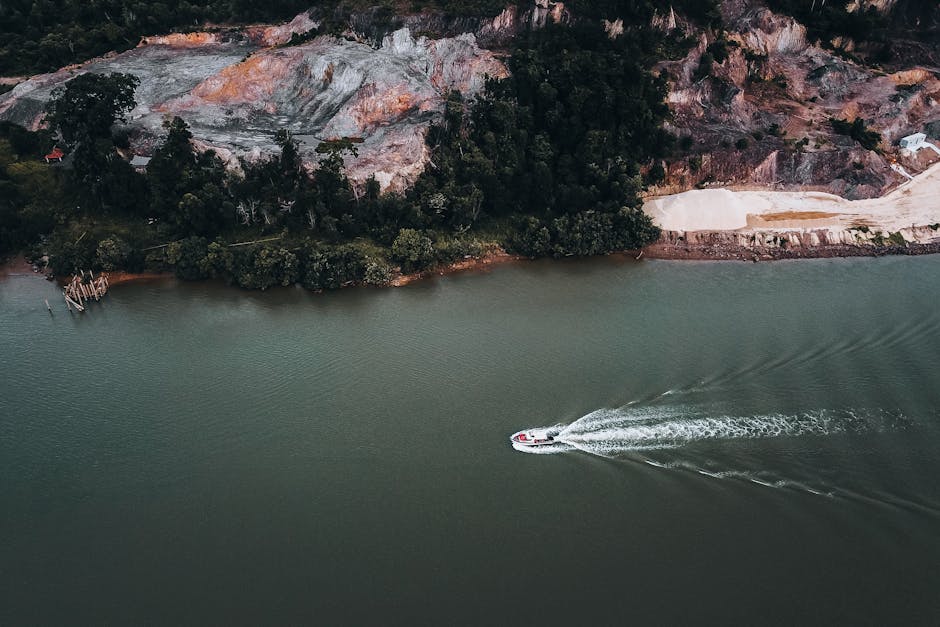 Immagine aerea di una barca che naviga su un fiume vicino a una costa, rilevanza con l'Atto di Navigazione e commercio marittimo.