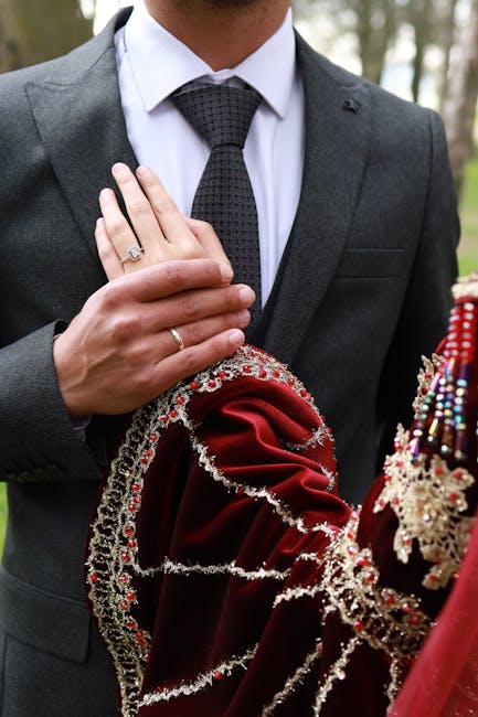 Dettaglio mani sposi con anelli e abito rosso ricamato, angoli coniugati nell'eleganza del design moderno e tradizione nuziale