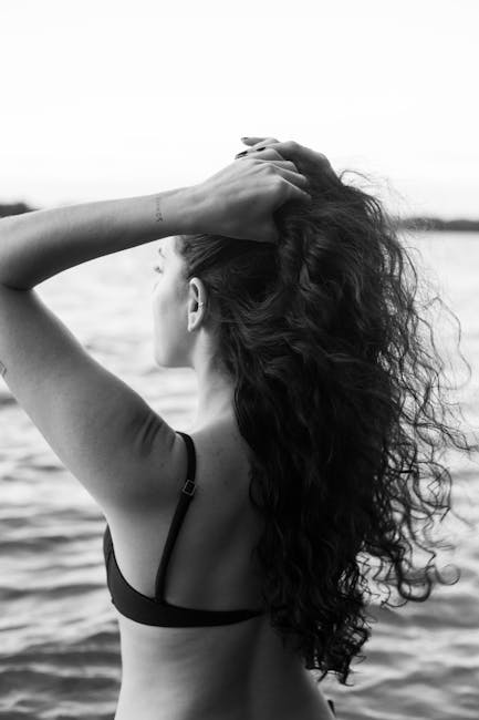 Donna di spalle al mare, capelli ricci e figura geometrica del corpo che ricorda una curva, in bianco e nero.