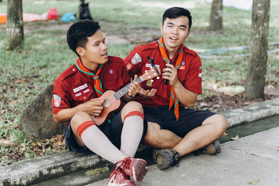 Ukulele e Amicizia: Attività Musicale Sorprendente Due amici scout suonano l'ukulele all'aperto, un'attività musicale stravagante e coinvolgente per sorprendere i tuoi amici.