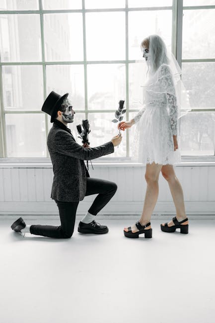 Proposta di matrimonio in stile Halloween: uomo in ginocchio offre rose nere a sposa con velo e trucco scheletrico.
