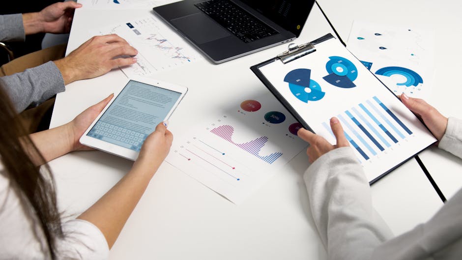 Team di lavoro analizza grafici e dati economici su tablet e documenti cartacei per lezioni di economia aziendale
