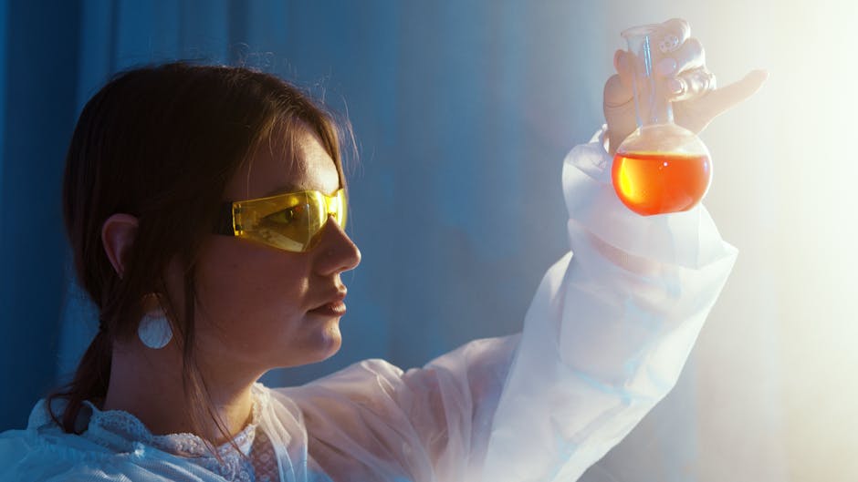 Scienziata con occhiali protettivi esamina liquido arancione in matraccio sferico, studio angoli adiacenti ad un lato e applicazioni
