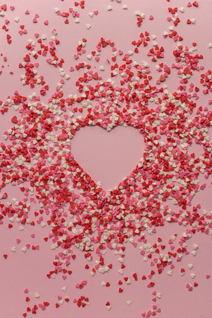 Confetti a forma di cuore rossi, bianchi e rosa su sfondo rosa, che creano una forma di cuore vuota. Metafora del tempo che passa.