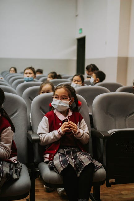 Studenti con mascherina in aula magna, attesa per la nuova scuola di Santa Eulària, anno scolastico 2027-28. Progetto educativo e futuro.
