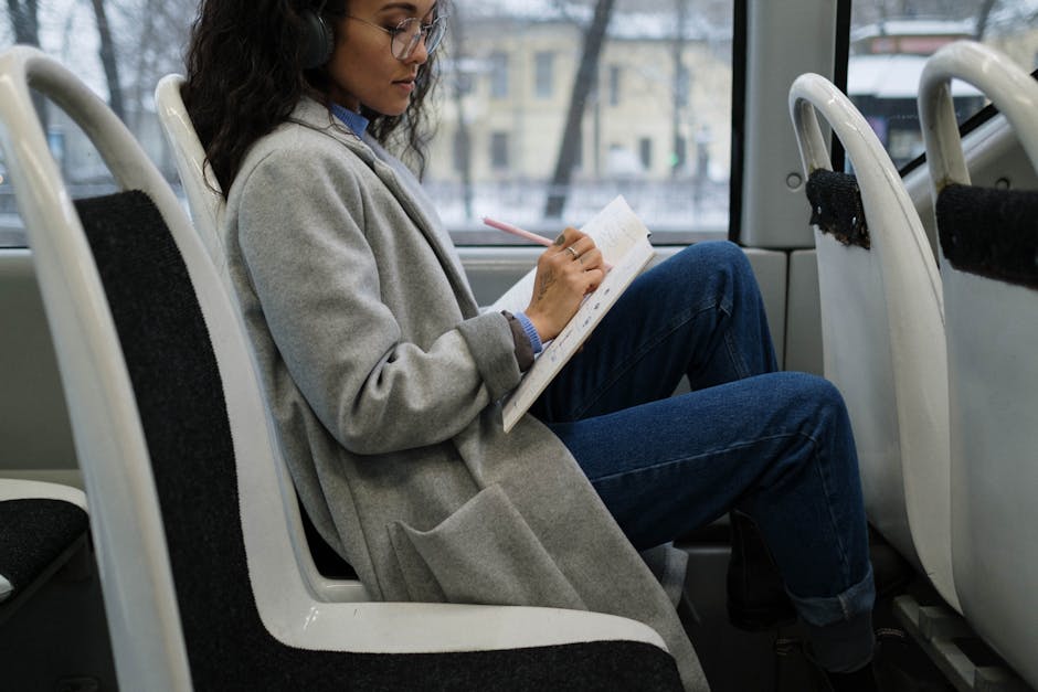 Donna con cuffie scrive spartiti musicali su un quaderno in treno, esempio di apprendimento musicale creativo e trasporto pubblico