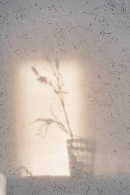 Ombra delicata di un fiore in vaso su parete chiara, metafora della bellezza effimera che risuona nel tempo come un capolavoro letterario.