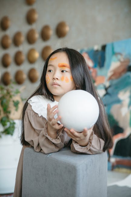 Bambina con pittura facciale arancione gioca con sfera bianca, attività ritmiche per bambini, sviluppo creatività e divertimento.