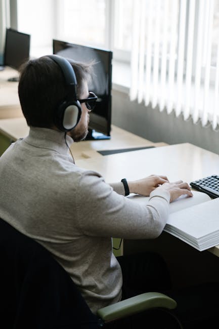 Studente non vedente con cuffie legge libro in braille al computer, simbolo di inclusione e pari opportunità nell'istruzione.