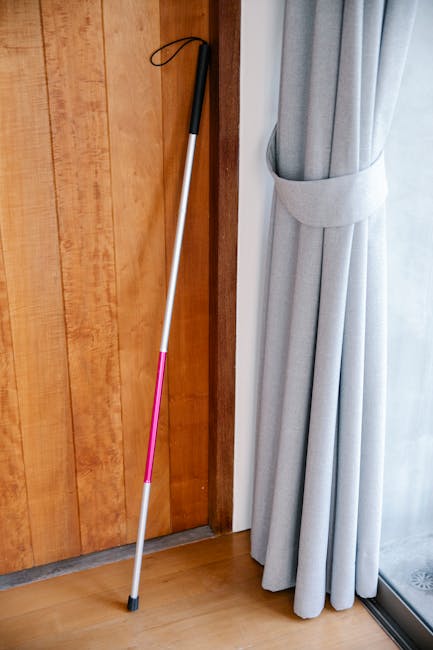 Bastone bianco appoggiato a porta in legno e tenda grigia, utile per persone con disabilità visiva, conversione ml grammi