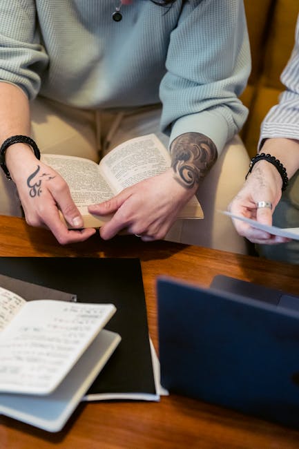 Studente che legge un libro con tatuaggi, simbolo di apprendimento e crescita personale nell'educazione online flessibile e accessibile.