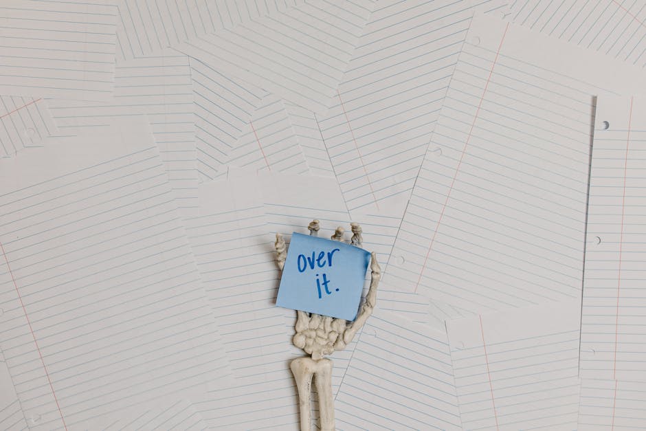 Mano scheletrica con post-it 'Over it' su sfondo di fogli a righe, simbolo di esaurimento nello studio di '1984'