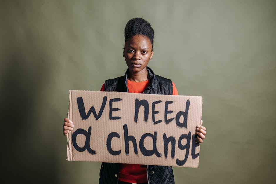 Donna afroamericana con cartello 'We need a change' che esprime la necessità di giustizia sociale e cambiamento reale.