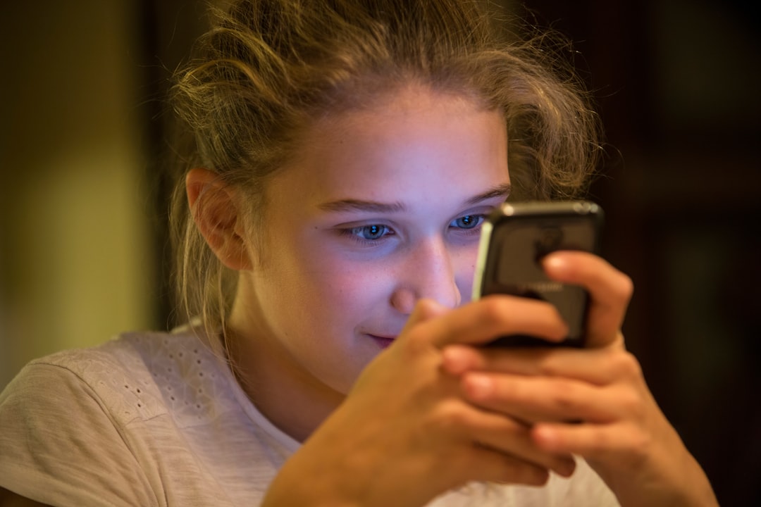 Ragazza sorridente usa smartphone al buio, Safer Internet Day 2026: chatbot supporto emotivo per giovani e benessere digitale.