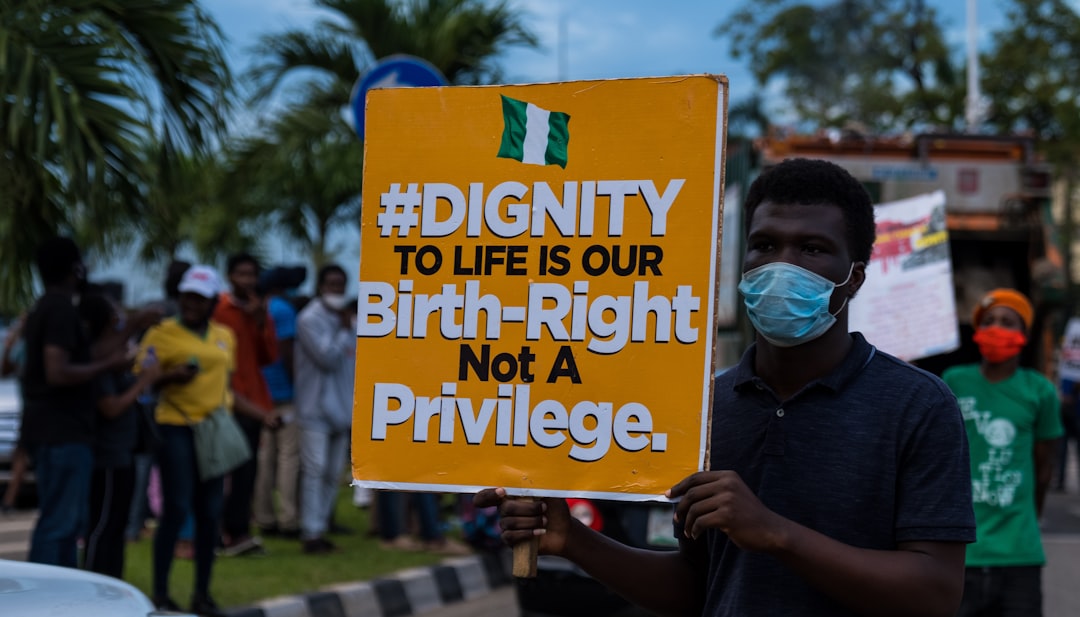 Manifestante con cartello Dignity to Life is our Birth-Right Not a Privilege e bandiera nigeriana, durante una protesta