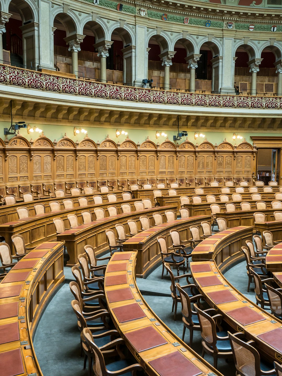 Aula parlamentare vuota con banchi in legno e sedie, discussione sulla ristorazione scolastica e iniziative didattiche in Parlamento